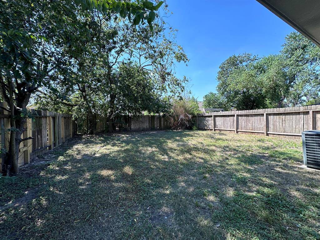 Spacious backyard with mature trees and a wooden fence, offering ample privacy and shade. Ideal for outdoor activities and gardening.