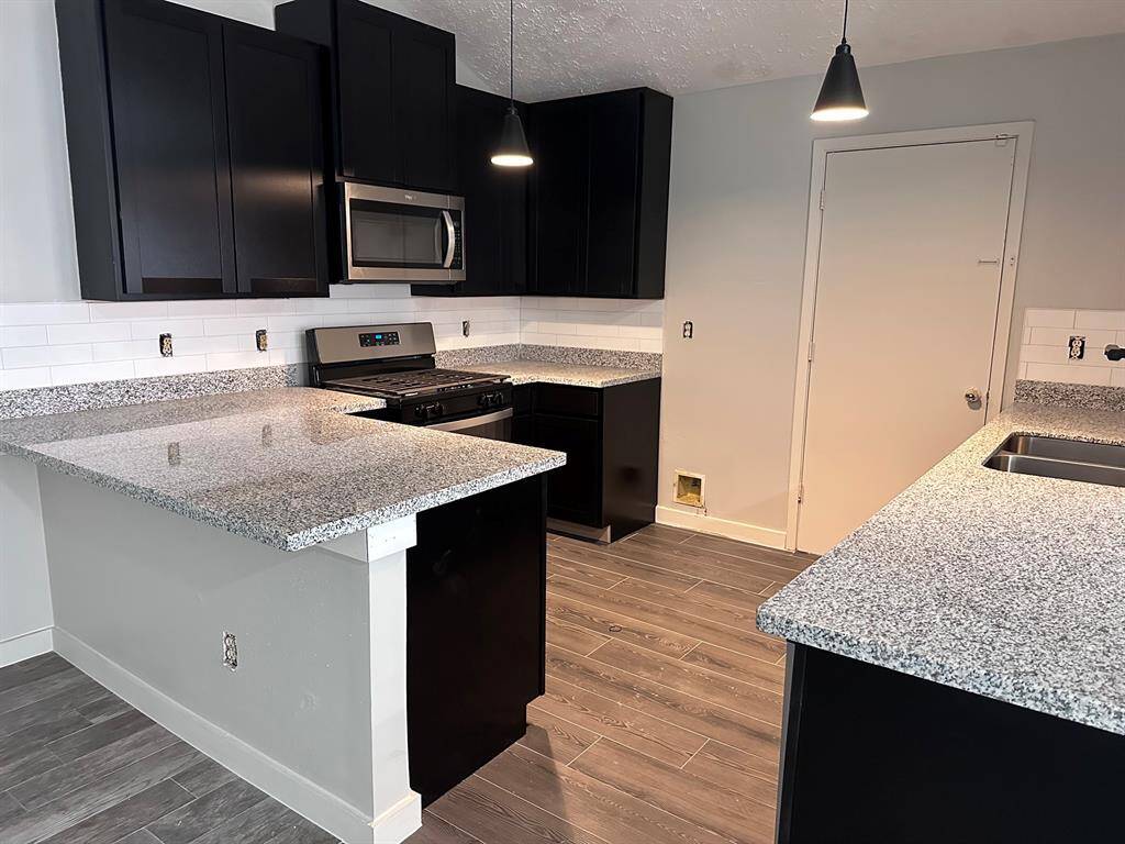 Modern kitchen featuring sleek black cabinets, granite countertops, stainless steel appliances, and a stylish tile floor. Bright and inviting with pendant lighting and a clean, contemporary design.