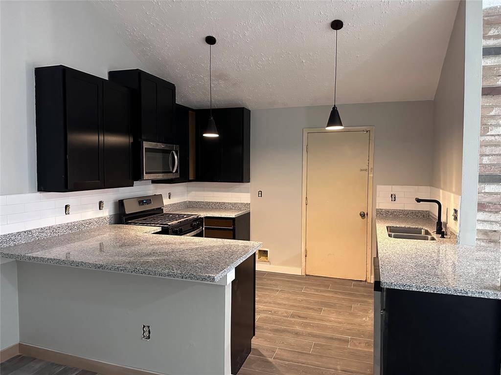 This photo showcases a modern kitchen with sleek black cabinets, granite countertops, and stainless steel appliances. The space features a breakfast bar, pendant lighting, and a neutral tile floor.
