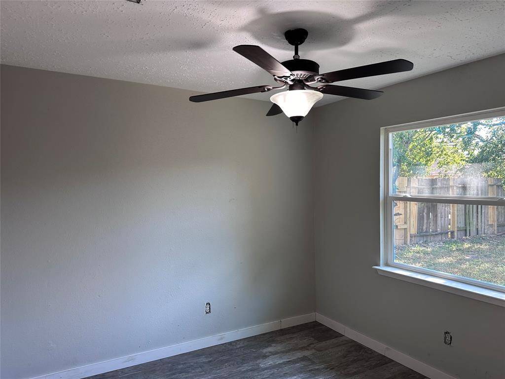 This room features a neutral color palette with light gray walls and wood-look flooring. It has a window providing natural light and a ceiling fan with a light fixture, offering comfort and modern style.