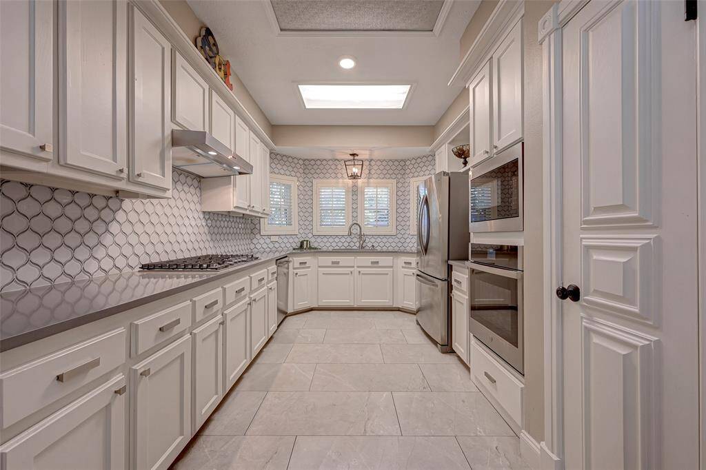The kitchen measures 15.0 x 9.0 and features a high ceiling for an airy feel. UPDATED IN 2020, its elegant white SHAKER-STYLE CABINETS are adorned with updated brushed nickel door hardware, adding a modern touch. The kitchen boasts a sleek grey QUARTZ COUNTERTOPS and is accentuated by ARABESQUE MOSAIC TILE BACKSPLASH, combining both style and functionality.