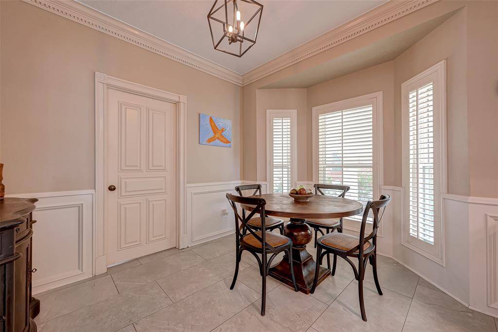 The breakfast room, measuring 11.11x8.10, offers a charming space with windows adorned with Plantation shutters, providing a pleasant view of the porte-cochère. Its continuous PORCELAIN TILE FLOORING is both stylish and practical, making cleanup a breeze, especially with little ones around. A convenient door from the breakfast room leads to the utility room. The home's QUALITY CRASFTSMANSHIP shines through in the doors, molding, and rosettes, adding a touch of timeless elegance throughout.
