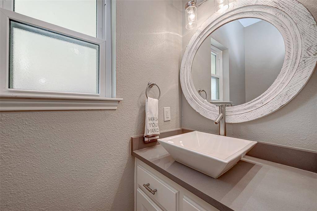The half-bathroom, conveniently situated off the utility room, boasts a stylish design with a quartz countertop, a sleek vessel sink, and a modern faucet. A decorative round mirror and updated Edison lighting add a touch of sophistication to this practical space.