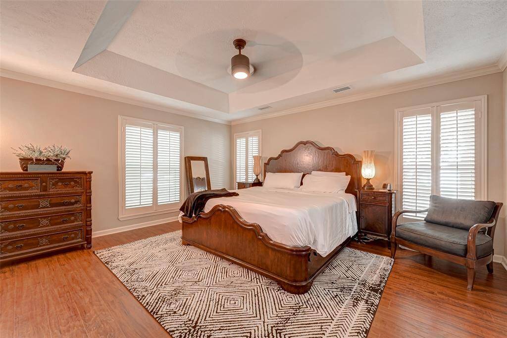 This home offers the luxury of two primary bedrooms, each with its ensuite bath. The first-floor owner's suite measures 16.0x15.4 and exudes classic traditional charm. PLANK-STYLE WOOD LAMINATE FLOORING adds a warm touch, complemented by a coffered ceiling with a ceiling fan. Windows adorned with Plantation shutters provide a tasteful view, and crown molding adds to the room's timeless appeal.