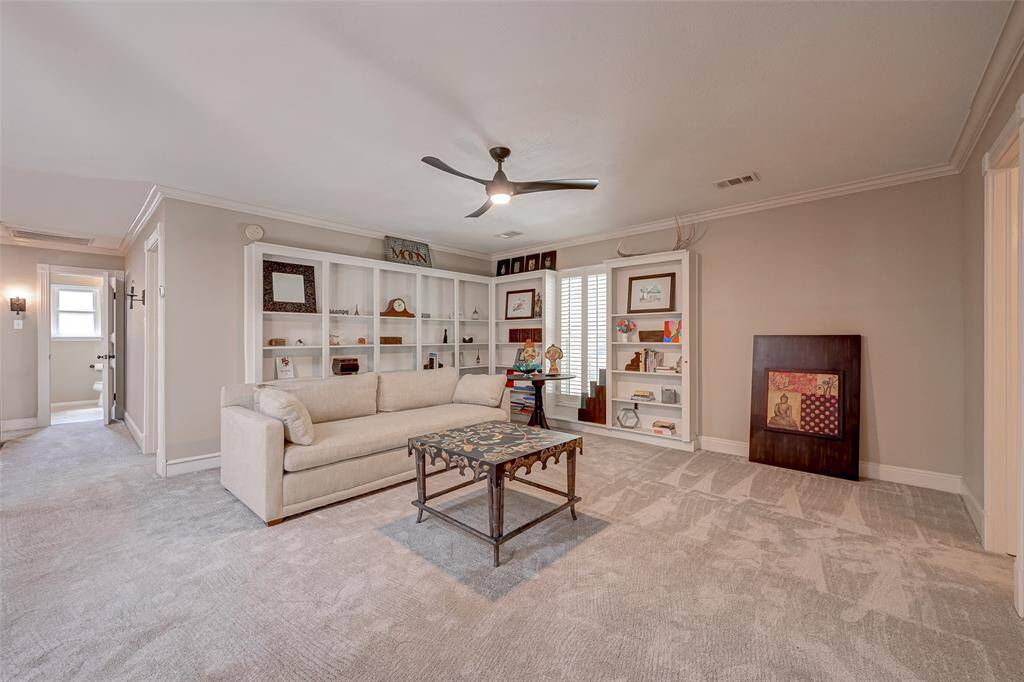 At the top of the stairs, you'll find a generously sized gameroom measuring 16.1x16.0. It features crown molding and a ceiling fan for added comfort. A wall of built-in bookcases adds both functionality and character. A window with Plantation shutters provides a delightful view of the front yard. This spacious room offers ample space for a sectional sofa and has wall space perfect for displaying a big-screen TV, making it an ideal spot for relaxation and entertainment.