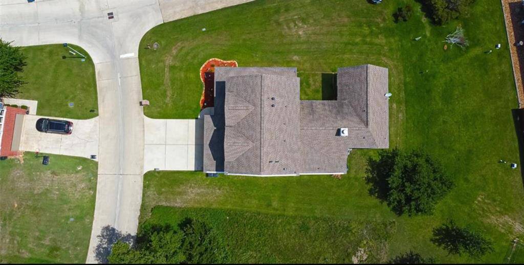 This aerial photo shows a view of the home situated on a spacious, well-maintained lawn. The property features a wide driveway leading to a garage, and the surrounding area is lush with greenery, providing ample outdoor space.