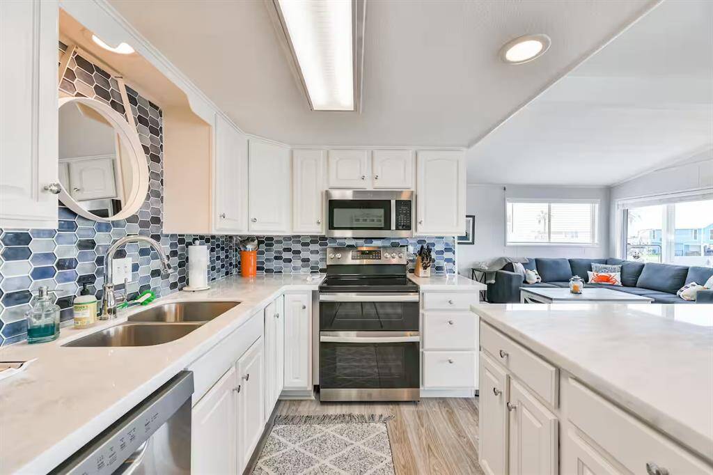 Bright, modern kitchen with white cabinetry, stainless steel appliances, and a stylish blue hexagonal tile backsplash. Open layout connecting to a cozy living area with ample natural light.