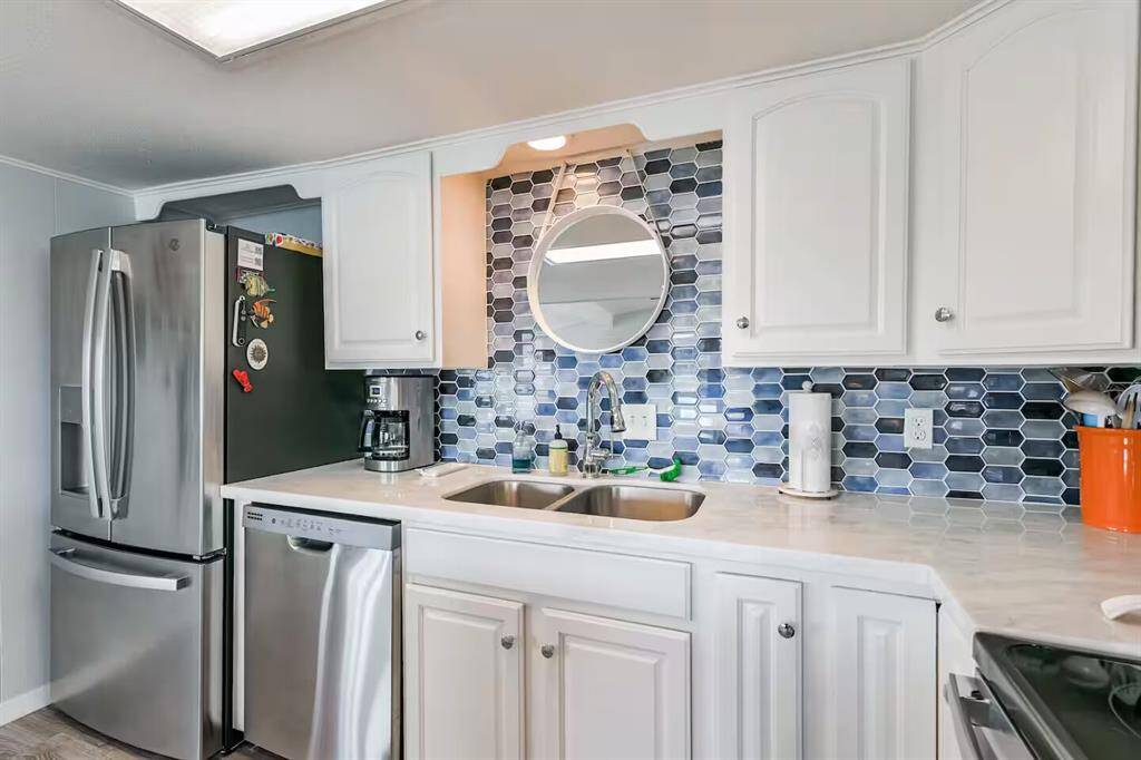 This modern kitchen features sleek stainless steel appliances, white cabinetry, and a stylish blue hexagonal tile backsplash. The space includes a double sink, ample counter space, and a cozy, contemporary vibe.