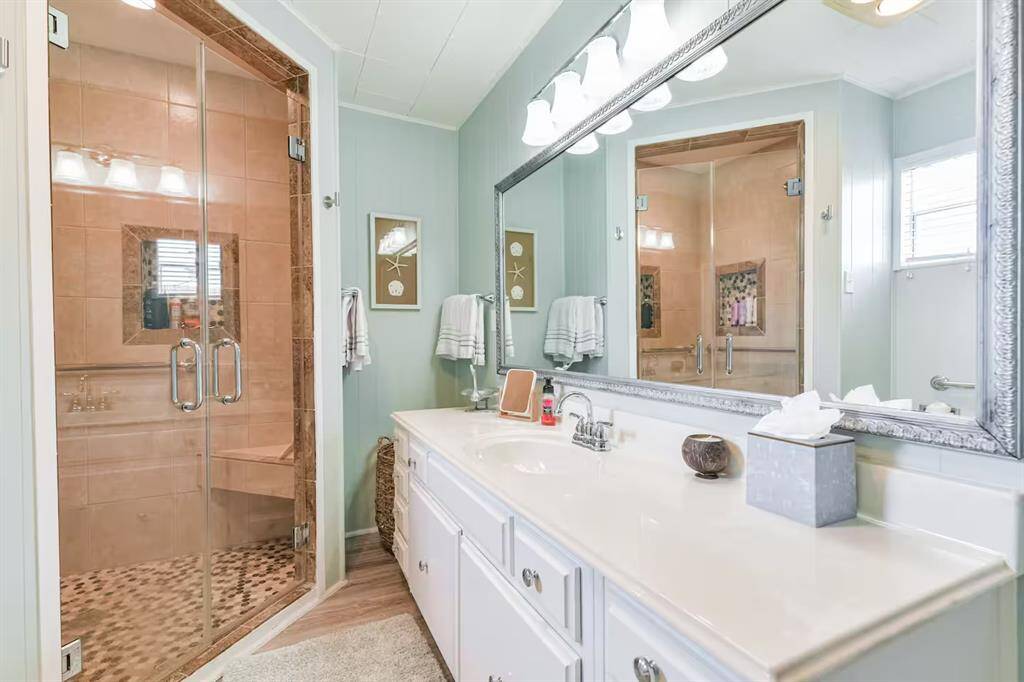 This bathroom features a spacious walk-in shower with glass doors and beige tiles. It has large vanity area with plenty of storage and a framed mirror, complemented by soft lighting and tasteful decor. The space feels bright and modern, offering comfort and style.