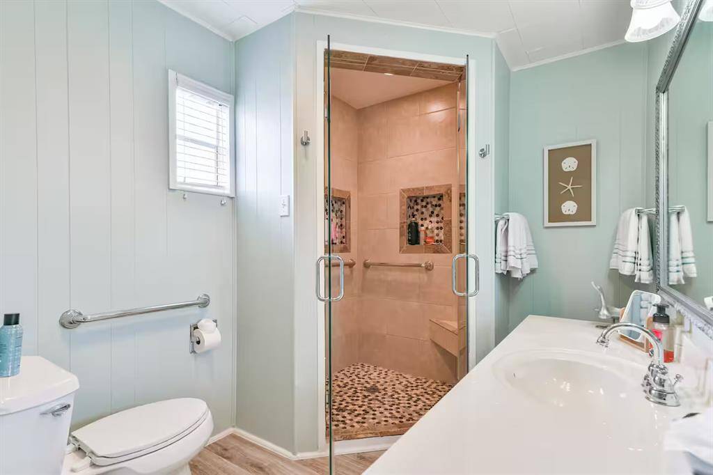 This bathroom features a sleek design with light blue walls, a spacious shower with a glass door and a white vanity with modern fixtures. A window allows natural light, enhancing the fresh and airy feel.