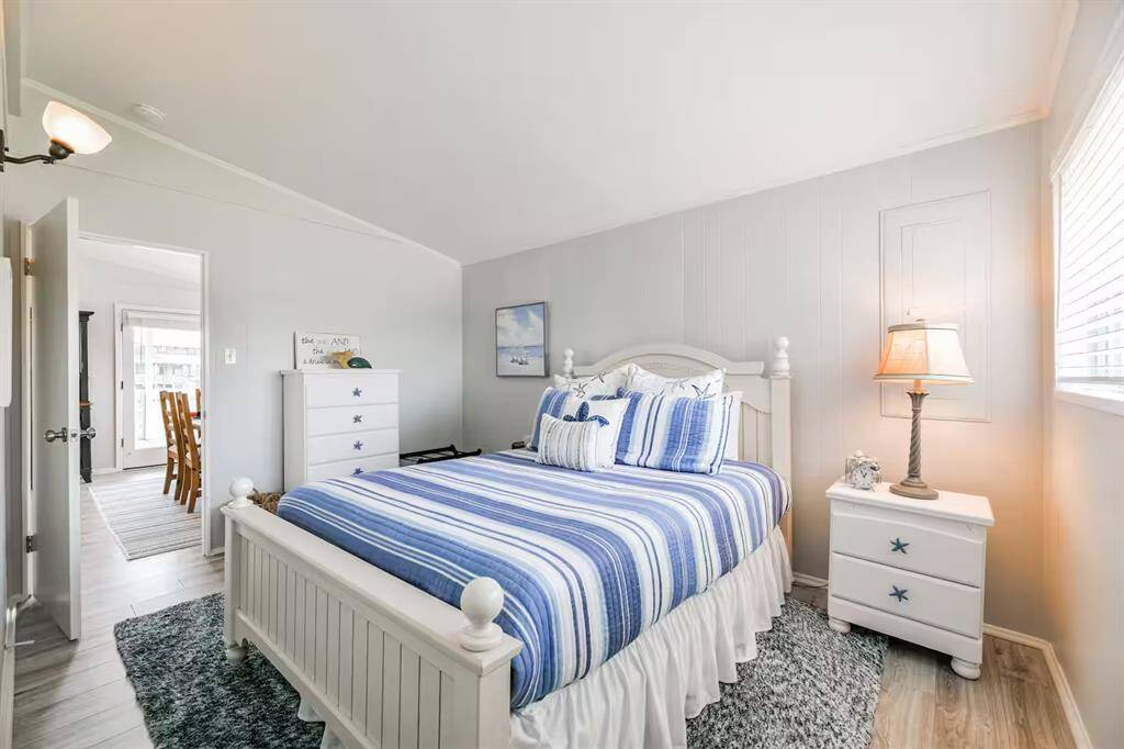 This cozy bedroom features a nautical theme with blue and white striped bedding, white furniture, and coastal decor. It has a bright, airy feel with light-colored walls and a window letting in natural light. A plush rug adds comfort, and there's ample storage with a dresser and nightstand.