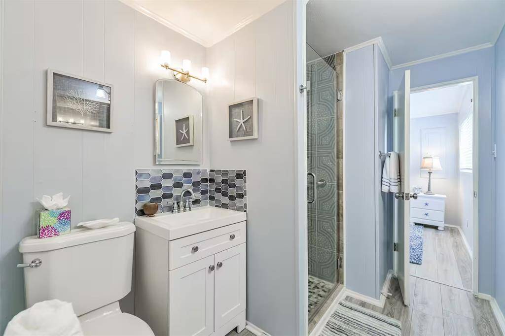 This bathroom features a clean, modern design with light blue walls, a white vanity, and a toilet. It includes a walk-in shower with a glass door and decorative tile.