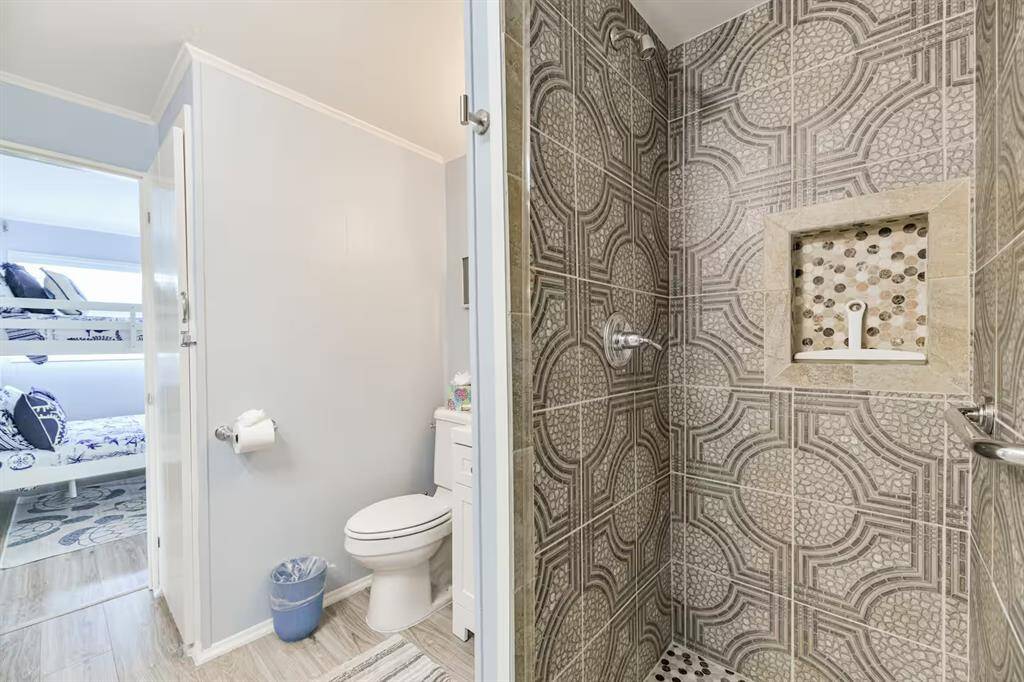 This modern bathroom is accented with patterned tile shower, built-in shelf, and adjacent toilet area. A glimpse of a bedroom with bunk beds is visible through the open door.