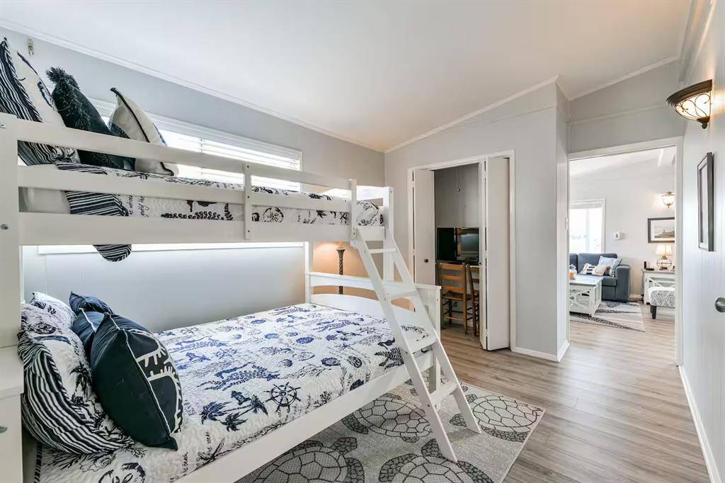 This bright bedroom features a bunk bed with nautical-themed bedding and leads into a cozy living area. The space is well-lit with natural light and has wood-style flooring, offering a welcoming and functional layout.