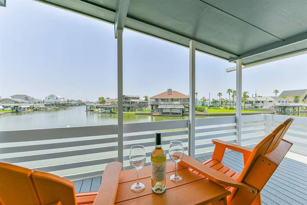 This photo showcases a serene waterfront view from a covered balcony, featuring comfortable seating and a small table perfect for relaxation. The picturesque canal setting is ideal for enjoying peaceful moments and outdoor gatherings.