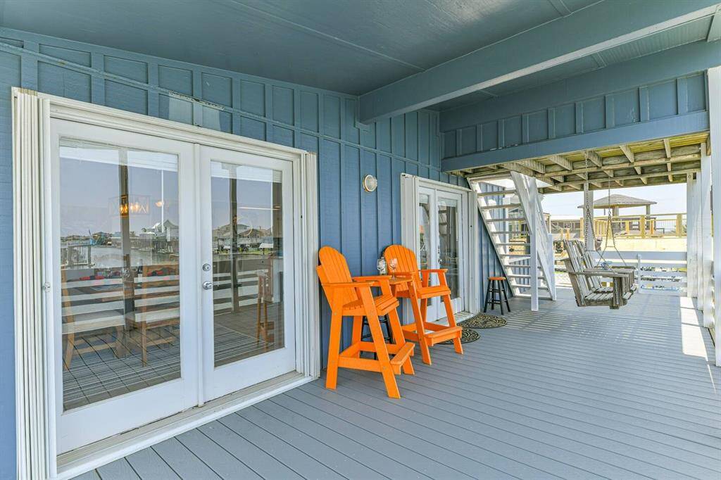 This photo showcases a spacious covered deck with vibrant seating and a swing, providing a relaxing outdoor space. The deck features double doors leading inside, and offers views of the surrounding area, ideal for enjoying the scenery.  The stairs lead up to the sun deck/crow's nest.