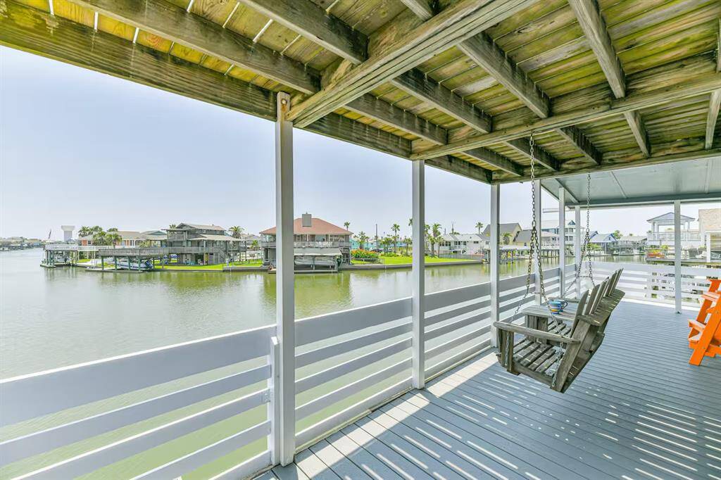 This photo showcases a spacious waterfront deck with a wooden swing and seating area, offering serene views of a canal.  Ideal for relaxation and enjoying the tranquil water setting. The vastness of the expansive canal brings you serenity.