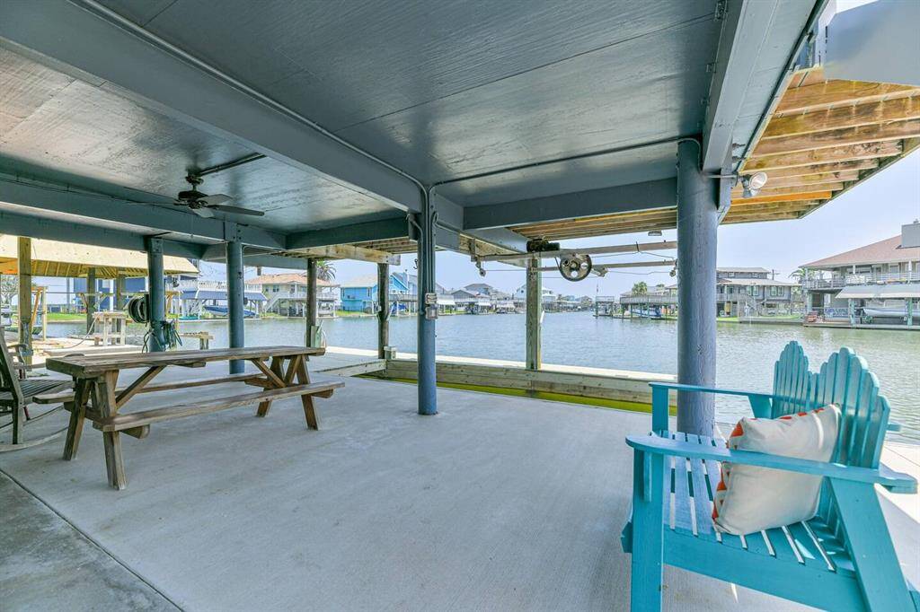 This photo showcases a spacious, covered outdoor patio overlooking a beautiful waterfront. It features a ceiling fan, picnic table, and colorful seating, ideal for relaxation or entertaining while enjoying the scenic water views. New boat dock, boat lift and fish cleaning table