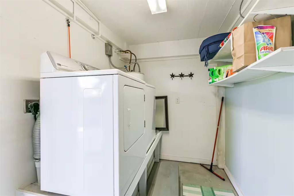 This photo features a compact laundry room with a washing machine and dryer. It has white walls, overhead shelving for storage, and a clean, organized layout suitable for household chores.
