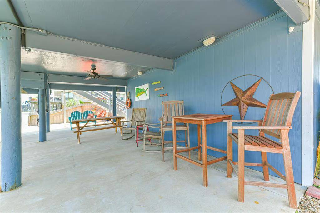 This photo features a spacious covered patio with a ceiling fan, wooden furniture, and vibrant decor, creating a cozy outdoor seating area perfect for relaxation and entertaining.