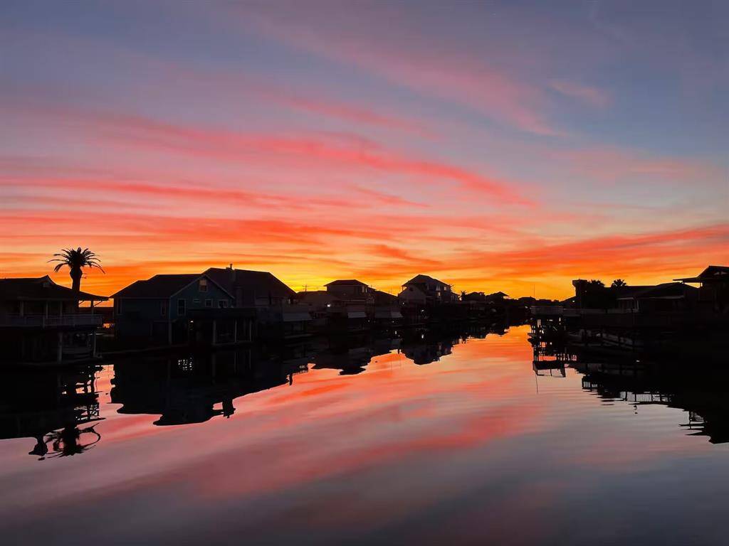 This photo captures a stunning waterfront view at sunset, featuring vibrant orange and pink skies reflecting on the calm water.