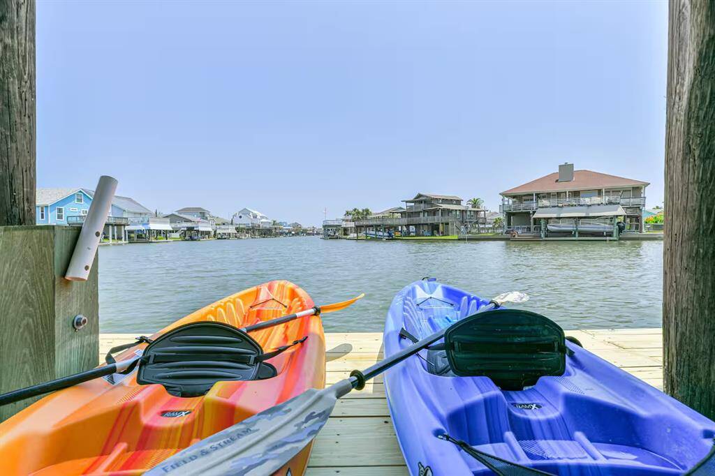 This photo showcases a serene waterfront view from a dock with two kayaks ready for use. The setting features nearby houses along the water, suggesting a peaceful residential area ideal for water enthusiasts.  So calm....on a wide canal.