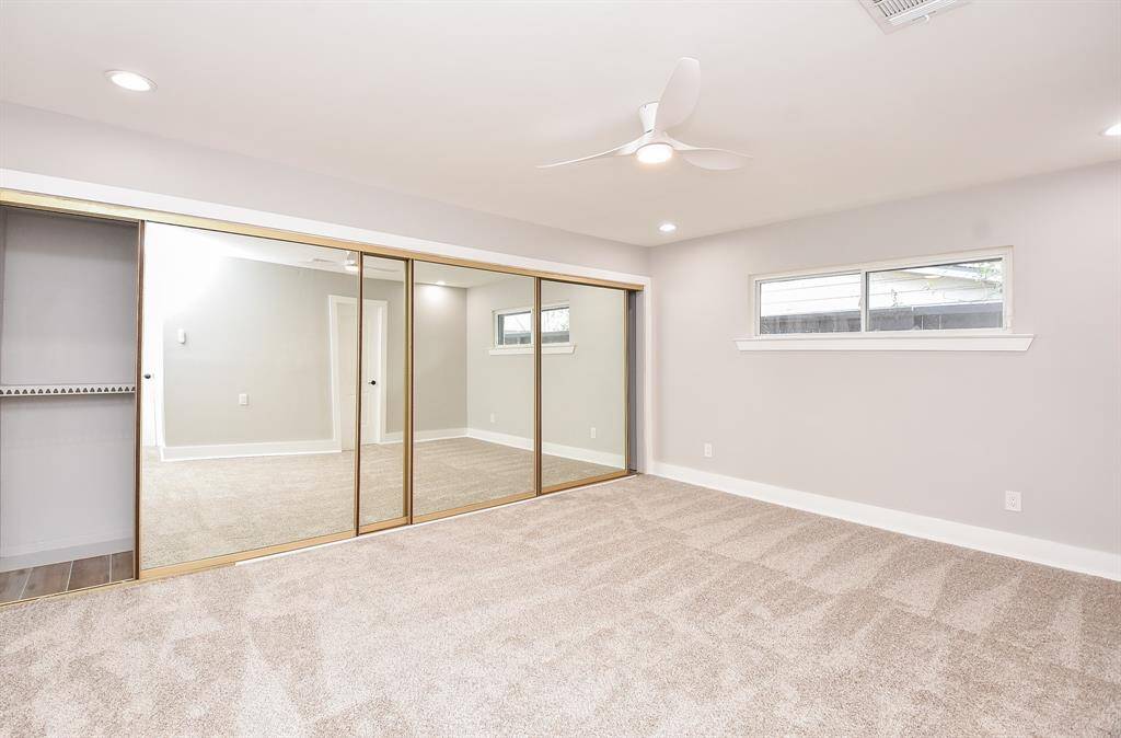Experience comfort in this primary bedroom featuring neutral carpeting, a ceiling fan, and recessed lighting. Enjoy the spacious mirrored closet and natural light from the window.