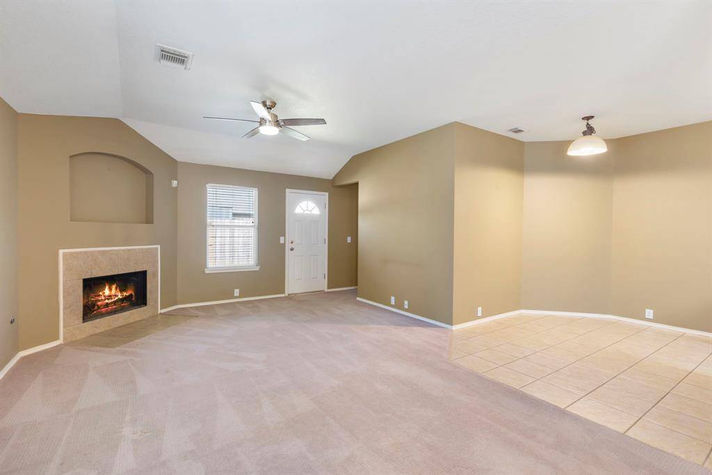 This spacious living area features neutral tones, a cozy fireplace, and a ceiling fan. It opens into a tiled dining area with ample natural light, creating a warm and inviting atmosphere.