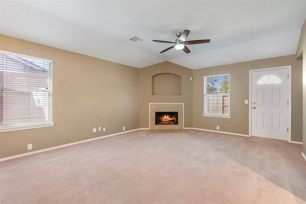 This spacious living room features a cozy fireplace, ceiling fan, and plenty of natural light from two large windows. The neutral walls and carpet offer a versatile backdrop for any decor style.