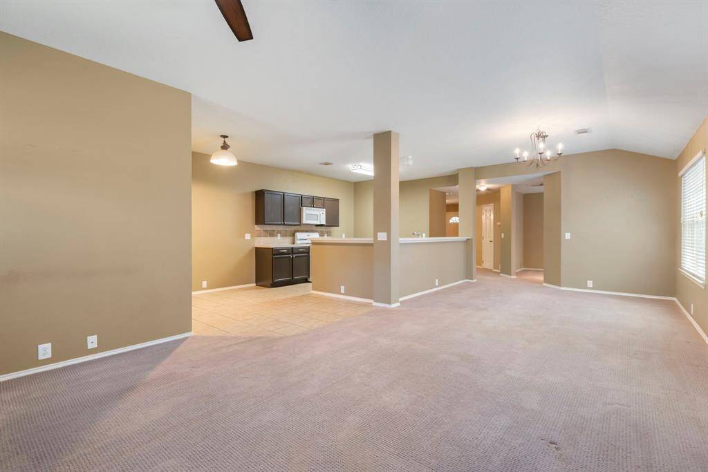 This spacious open-concept living area features neutral walls, plush carpet, and ample natural light. The adjacent kitchen includes dark cabinetry, a tiled floor, and a convenient bar counter, perfect for entertaining.