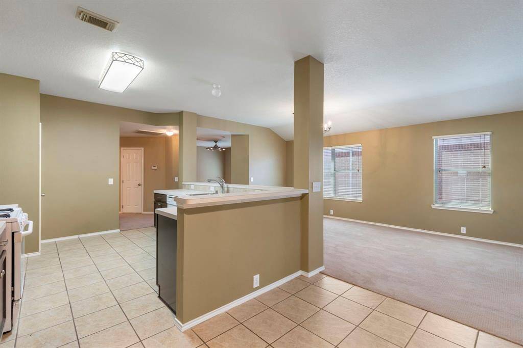 This photo showcases a spacious open-concept living area with a tiled kitchen and dining space, leading to a carpeted living room. It features large windows for natural light, neutral wall colors, and modern lighting fixtures.