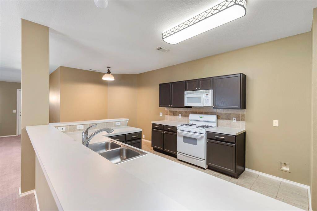 This kitchen features dark cabinetry, a white countertop with a double sink, a gas stove, and a microwave. The space is well-lit and open, providing a modern and functional cooking area.