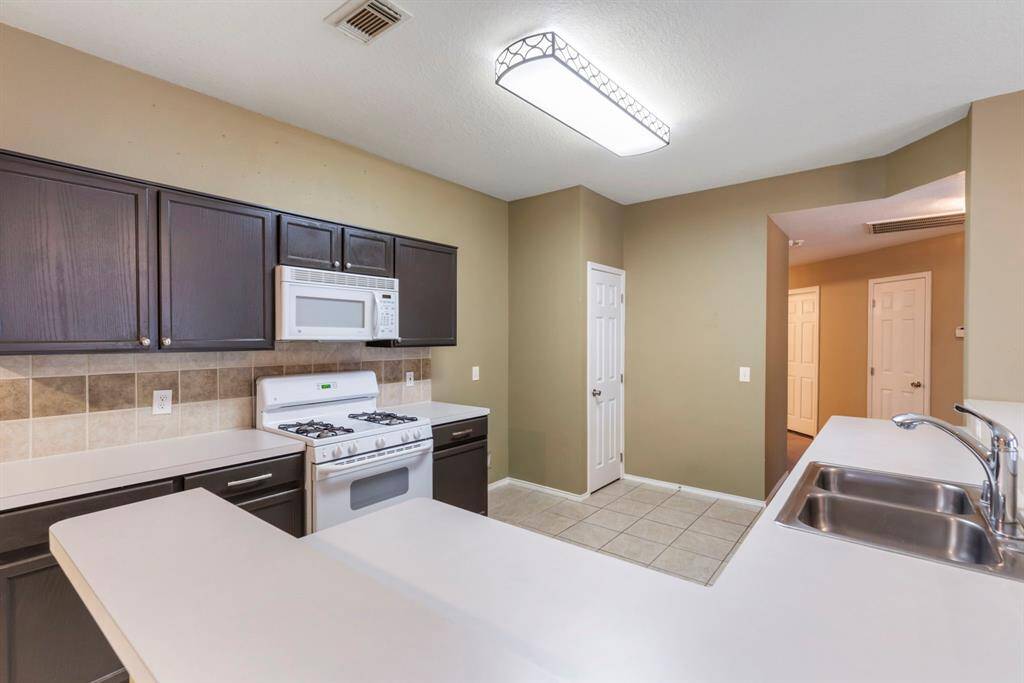 This kitchen features dark cabinetry, a gas stove with a built-in microwave, and a dual sink on a spacious countertop. The tile backsplash complements the neutral walls, and there's ample overhead lighting.