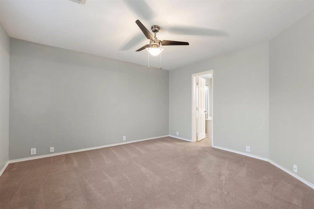 This room features a neutral-toned carpet and walls, a ceiling fan with a light fixture, and an entryway leading to what appears to be a bathroom. It's a spacious and versatile area suitable for various uses.