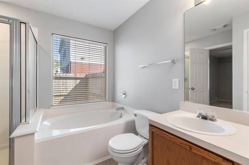 This bathroom features a spacious bathtub, a separate shower, a single-sink vanity, and a large window for natural light, creating a bright and inviting space.