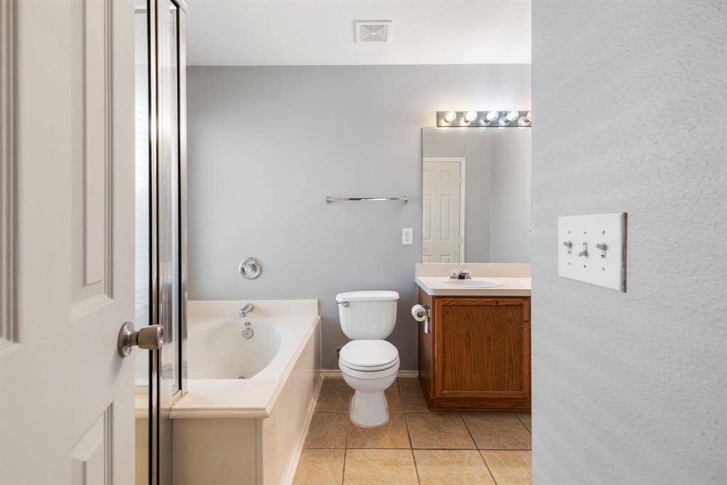 This bathroom features a clean, modern design with neutral tones. It includes a bathtub, shower, toilet, and a vanity with a mirror and lighting. The space is bright and functional.