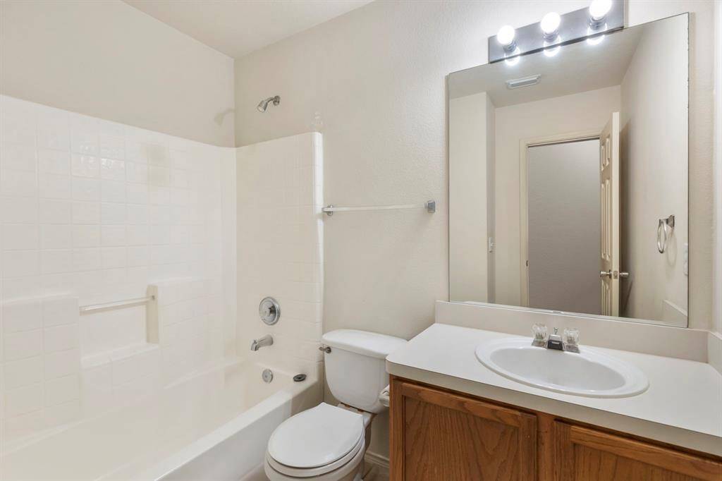 This bathroom features a clean and bright design with a combination shower and bathtub, a large mirror above a single-sink vanity with wood cabinetry, and modern lighting fixtures.