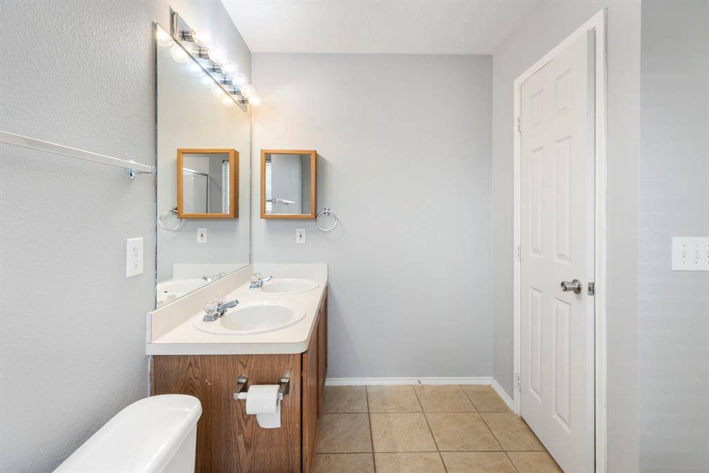 This bathroom features a double vanity with wooden cabinets, large mirrors, and modern lighting. It has neutral tile flooring and a clean, minimalist design, perfect for a contemporary home.