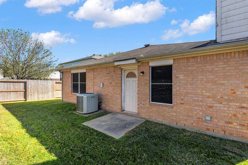 This photo shows a cozy backyard with a brick exterior, fenced yard, and concrete patio space. It includes a central air conditioning unit, offering a low-maintenance outdoor area ideal for relaxation.