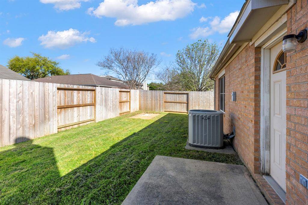 This photo shows a cozy backyard with a well-maintained lawn, bordered by a wooden privacy fence. The exterior features brick walls, a concrete patio area, and an HVAC unit, offering a practical outdoor space.
