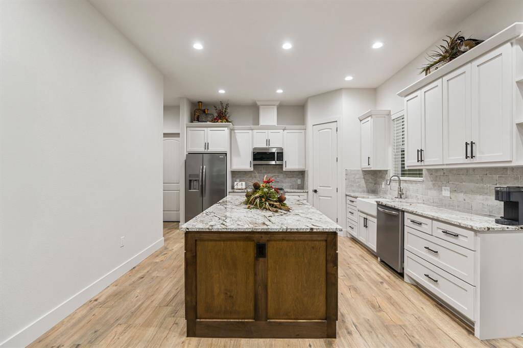 Kitchen features a granite island, white cabinets, stainless steel appliances, and recessed lighting.