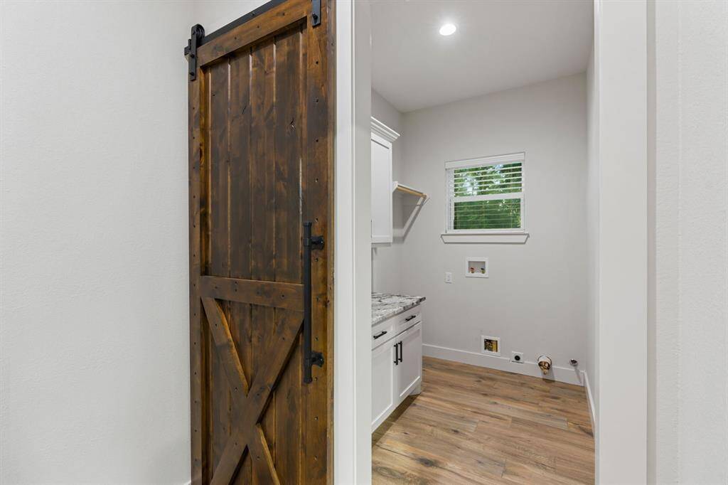 The laundry room behind a sliding barn door features granite counters, cabinets, and washer/dryer connections.