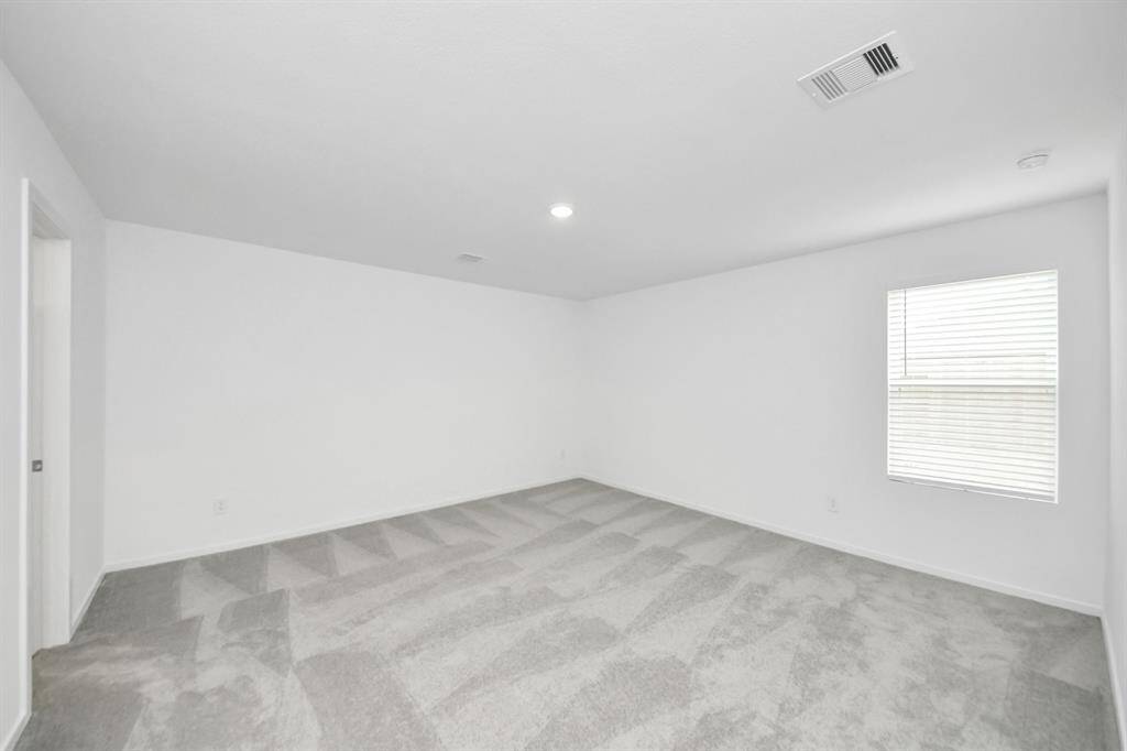 The primary bedroom features neutral carpeting, white walls, and ample natural light from a window.