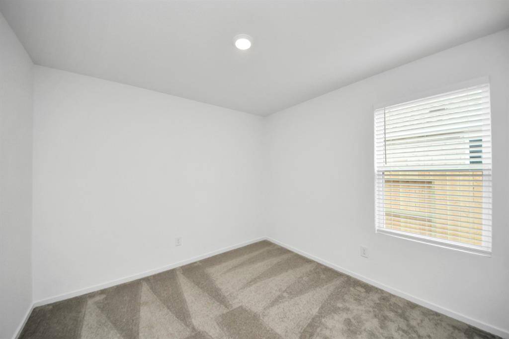 This is a bright room with white walls, a single window with blinds, and gray carpet. Ideal for a bedroom or office space.