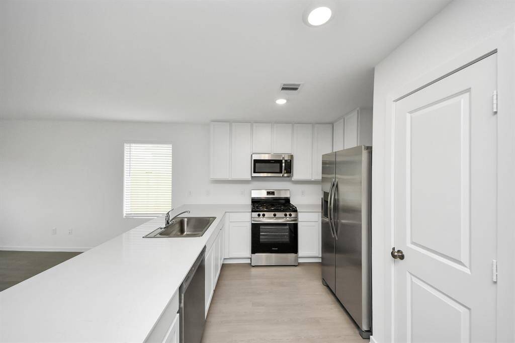 Modern kitchen with sleek white cabinetry, stainless steel appliances, and a breakfast bar with a sink.