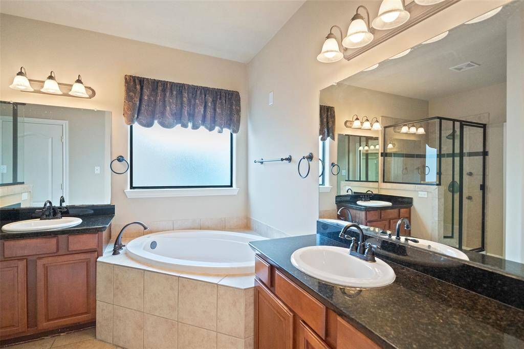 Experience spa-like luxury in this en-suite bathroom, boasting his-and-her vanities, sleek bronze fixtures, a sumptuous garden tub, and a spacious walk-in shower.
