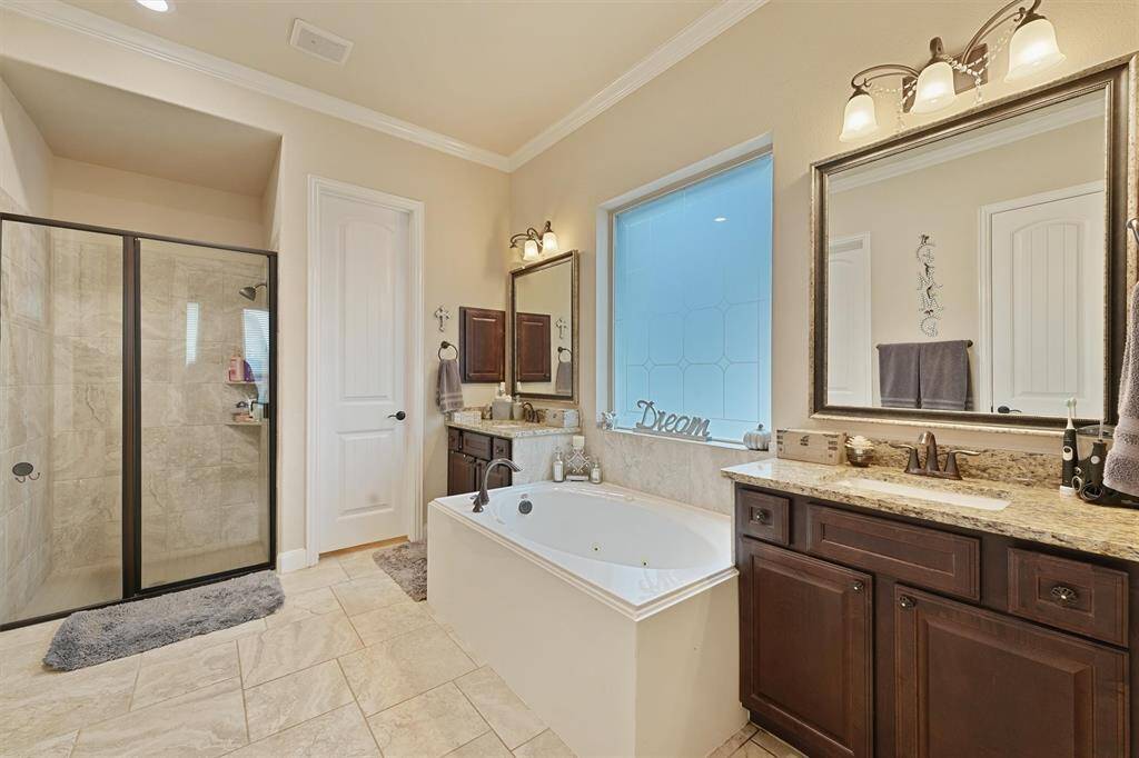 This bathroom features a spacious layout with a large glass-enclosed shower, a soaking tub, double sinks with granite countertops, and elegant lighting. The natural stone tile floor and neutral color palette create a luxurious and inviting atmosphere.