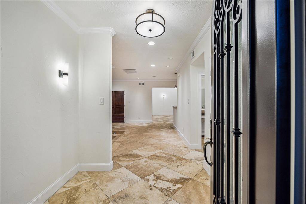 FOYER… An impressive wrought iron door with openable frosted glass gives entry directly to the living room (left), dining room (front), and kitchen (right) in open concept style. High ceilings, over-sized 2’ x 2’ travertine flooring, and tastefully placed wall sconces elevate the space.  Not pictured is downstairs guest half-bath on the right of the foyer.