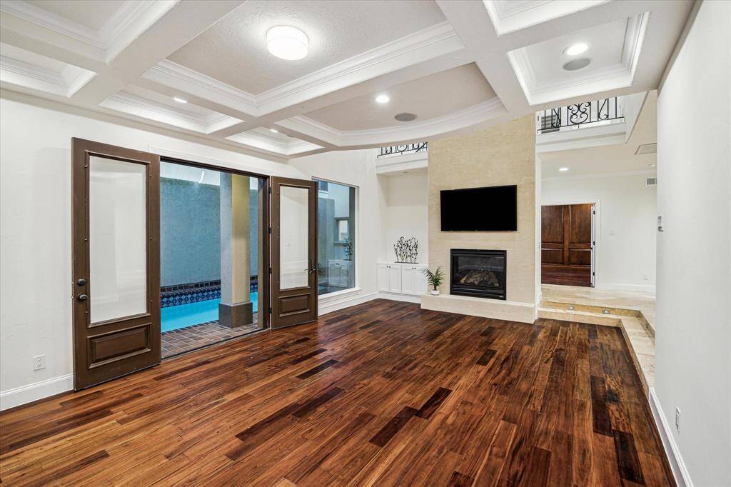 FORMAL LIVING ROOM… As you step down into the living room pass by the two-story grand gas log fireplace and step down onto the warm-toned wood floor. Features a built-in bookcase, coffered ceiling, crown molding and French doors that lead to the pool/spa area. Over-sized windows provide fantastic natural light.