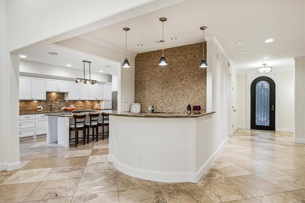 WET BAR… Granite counters, decorative travertine backsplash, custom cabinetry, stainless undermount sink, decorative pendant lighting and Danby Silhouette wine refrigerator. The multi-tiered bar counter looks onto the living room allowing easy socialization while mixing.